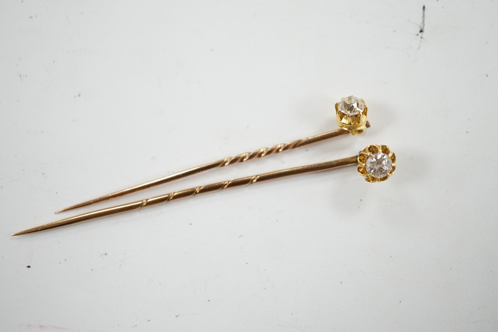 Two early 20th century yellow metal and solitaire diamond set stick pins, 65mm and a dress stud. Condition - fair to good